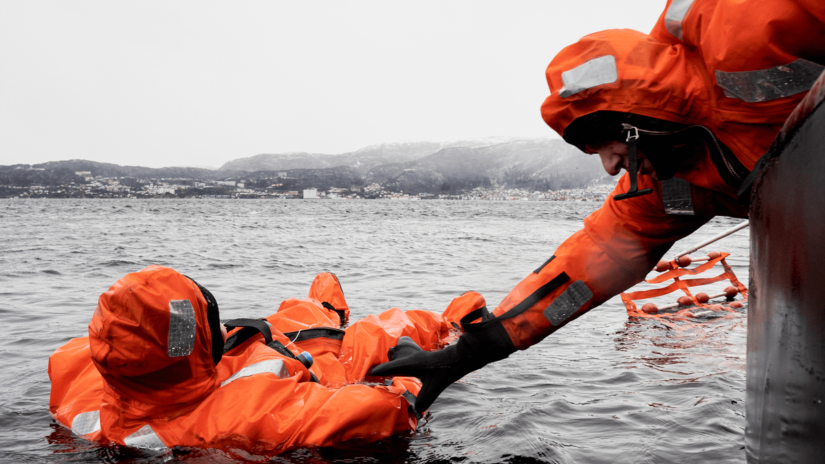 En person i oransje overlevelsesdrakt i vannet blir hjulpet opp av en person fra en båt, under en øvelse.
